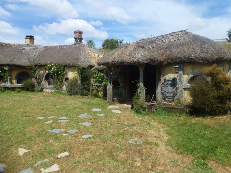 the pub in hobbiton in a tudor style with thatched roof and yellow walls, there is a path through the grass to the door