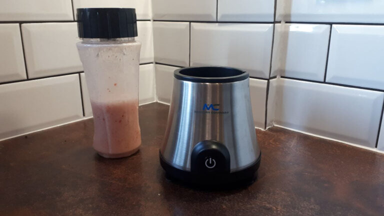 a blender on a dark brown worktop, there is a silver base of the blender and the top part has been blended and is pink
