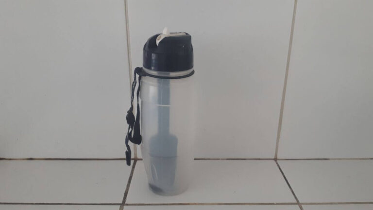 a clear water bottle with a filter inside and a wrist band stood in some kitchen tiles