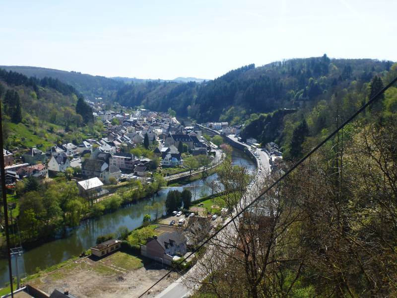 a few looking down on a valley with a river running through the middle, on one side a lot of buildings and on the other side a road, on the hills around the valley are a lot of trees