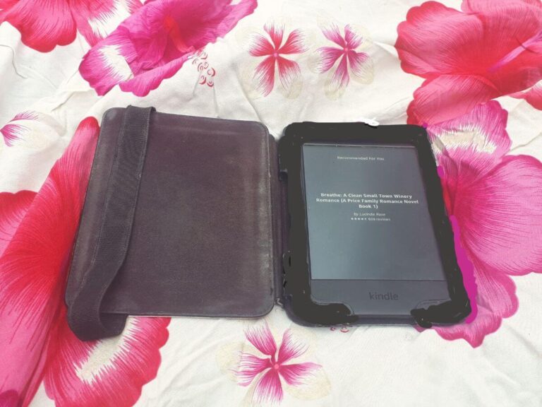 a kindle with a cover laid on a white blanket with pink flowers