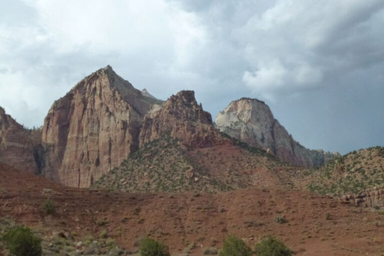 White and orange cliffs in the background, with orange hills in the foreground and a few green bushes growing on the slopes