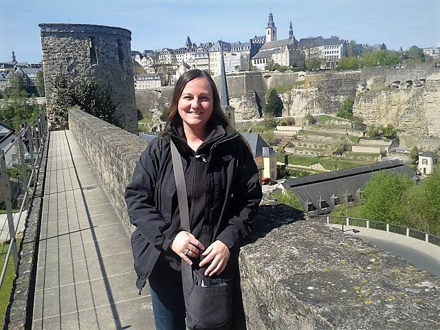 a girl dressed in black, stood on an old wall with a city in the background next to a valley, with lots of houses