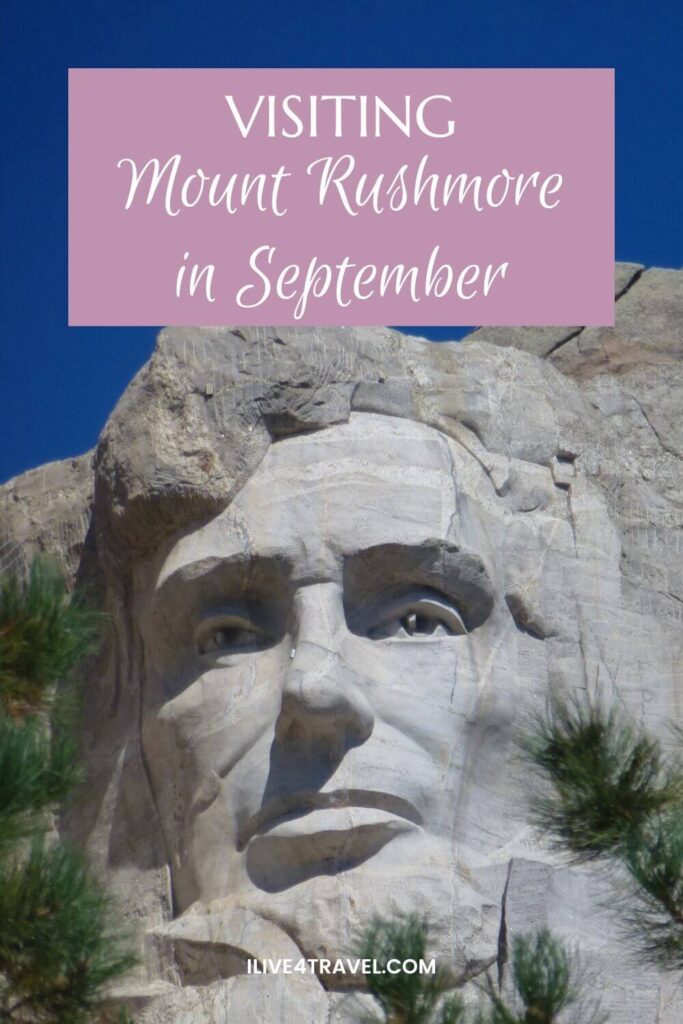Pinterest pin showing a close-up of Abraham Lincoln’s face carved into Mount Rushmore, with fine details of the stonework highlighted against a clear blue sky. Green pine branches frame the bottom edges of the image. The pin text reads “Visiting Mount Rushmore in September"