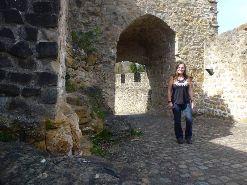 a girl with a black tshirt and jeans, standing in the entrance of a stone castle