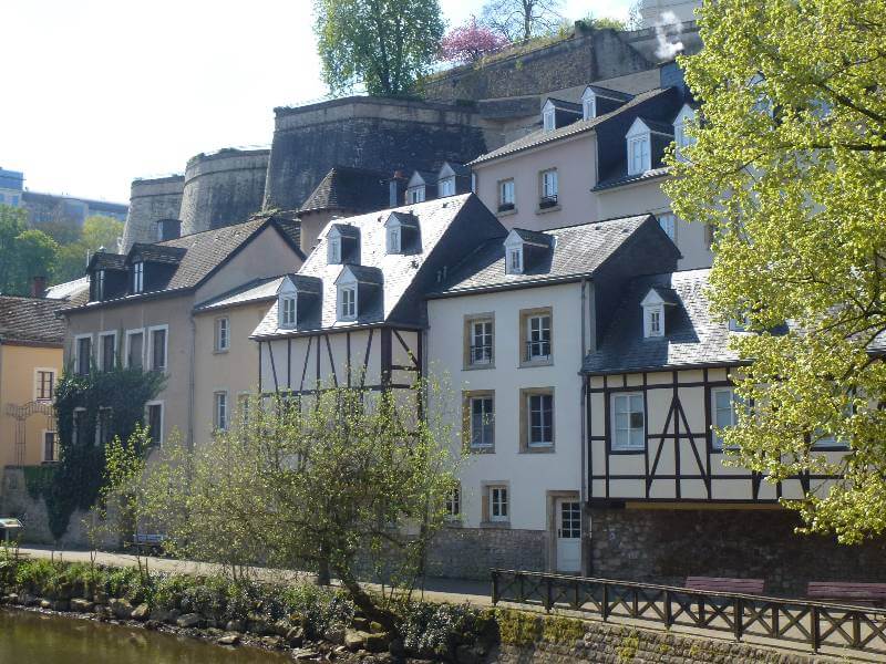 buildings alongside the river with a stone wall behind them and a few trees