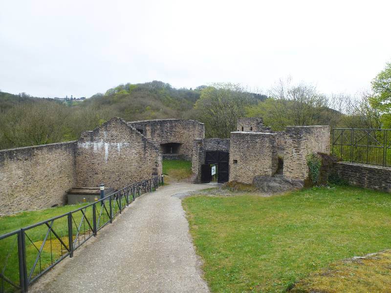 ruins of the gate entrance of a castle with grass and a fence and trees in the background