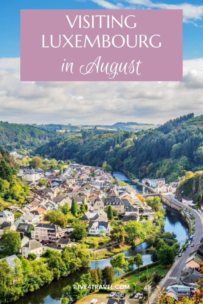 a pinterest pin about visiting luxembourg in august, showing a valley with a river running through it, a road and hill covered in trees to the right and houses to the left