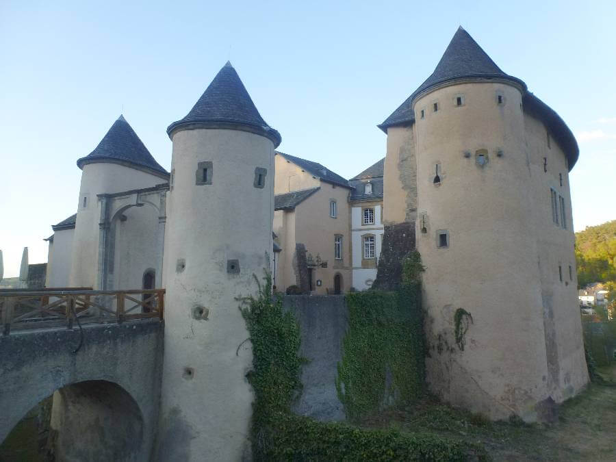a castle with round turrets and a light colour and a bridge over to the castle