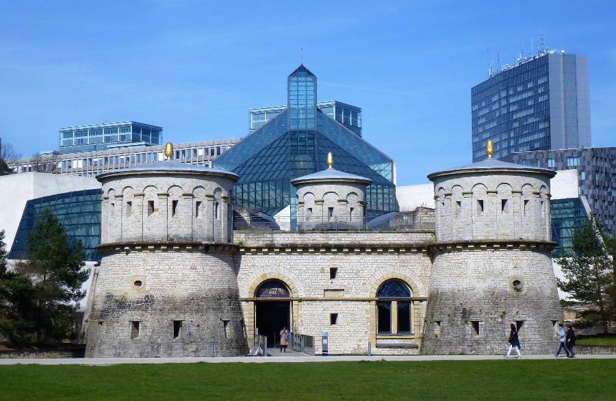 a castle with round turrets and modern glass buildings behind it