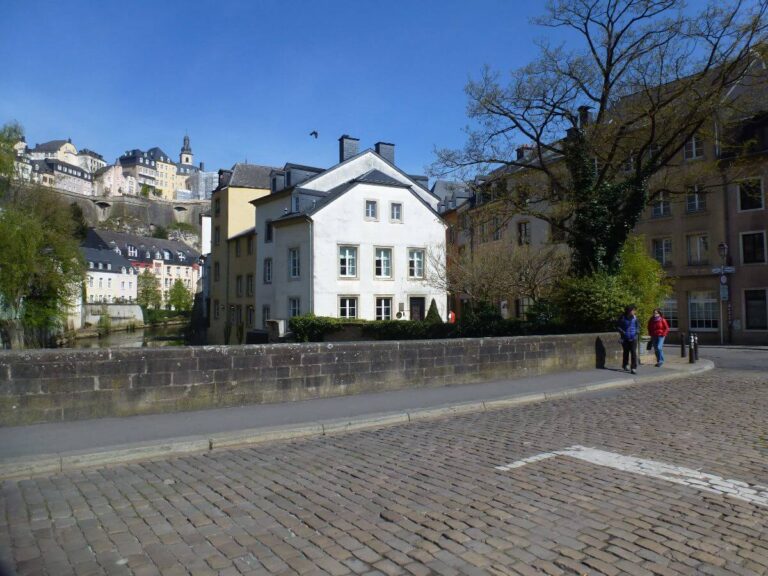 a road with a white building at the other side with other buildings behind it