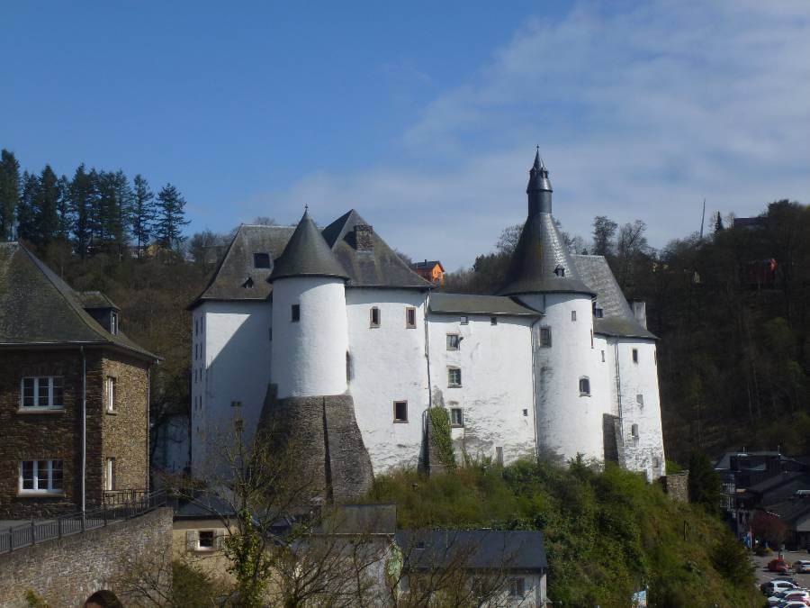 a white castle above a town with some buildings to the left and below and trees behind
