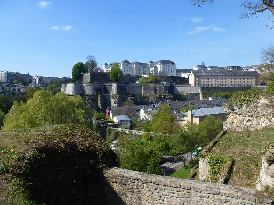 a view across a valley of houses in the valley, a wall around the valley and buildings on the top, there are also a lot of trees in the valley