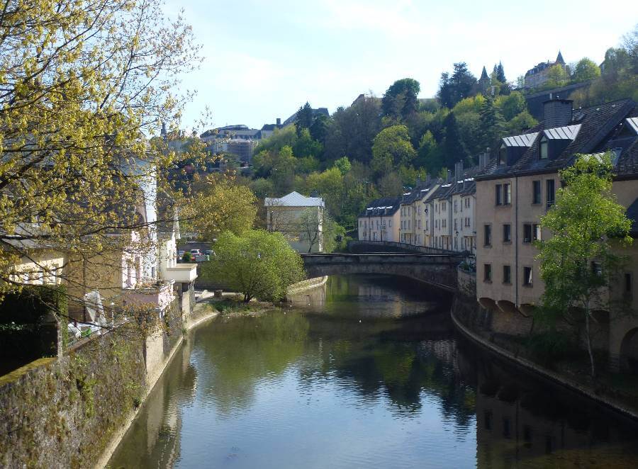 a river with buildings to the side of it, with a few trees on the sides and trees in the background