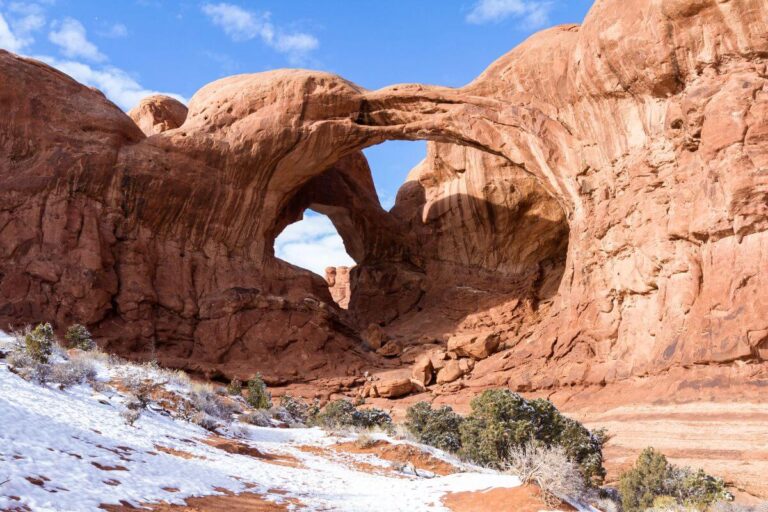 an arch in a very large orange rock formation, with snow on the ground