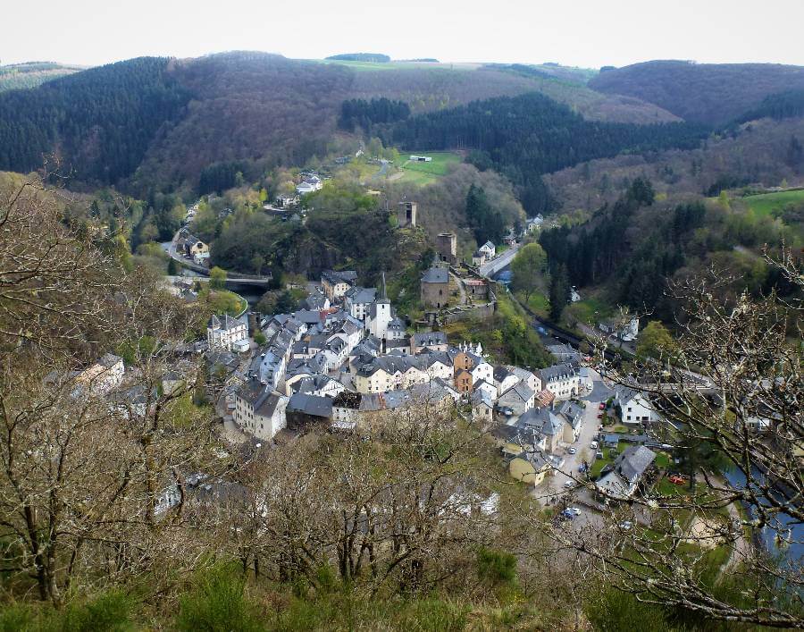 a small town surrounded on three sides by a river with a castle on top of a hill in the town, with fields and trees on the hills around it