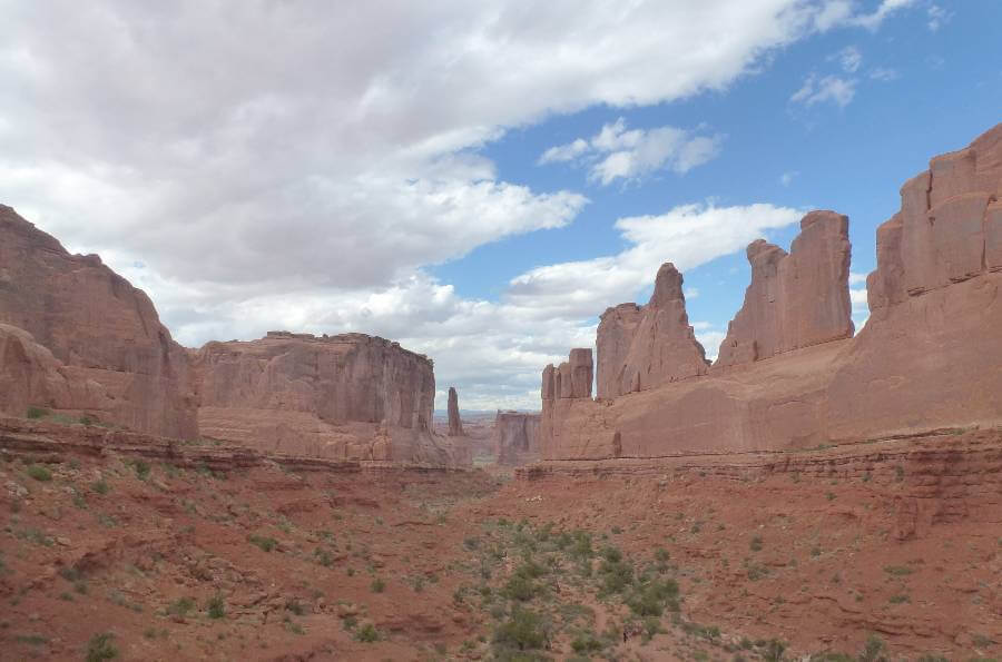 a large flat piece of land with huge weathered rock formations on either side of the image, with parts worn away by erosion, the rocks and the ground are a red color