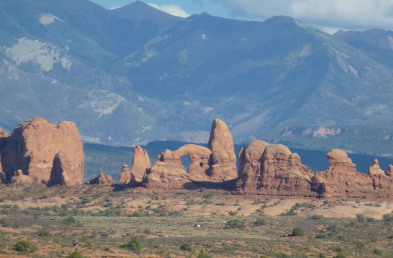 an image of different orange rocks in a flat valley, one of them has an large in it, with mountains in the background
