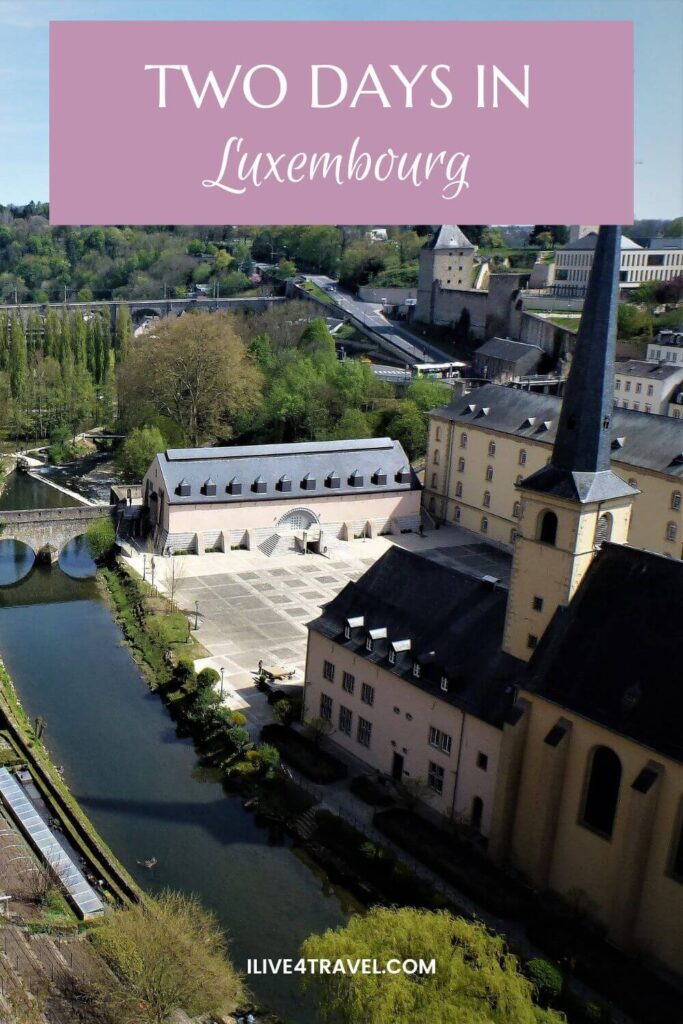 a pinterest pin about spending 2 days in luxembourg showing a river flowing through a valley with buildings next to it, a hill in the background with trees on it and a railway bridge
