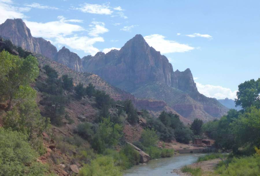 zion canyon with the river running through it and trees on the slopes leading down to the river and the canyon sides in the distance