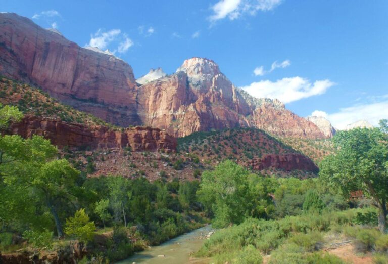 a river running through a canyon, with the orange canyon walls in the distance and trees on either side of the river