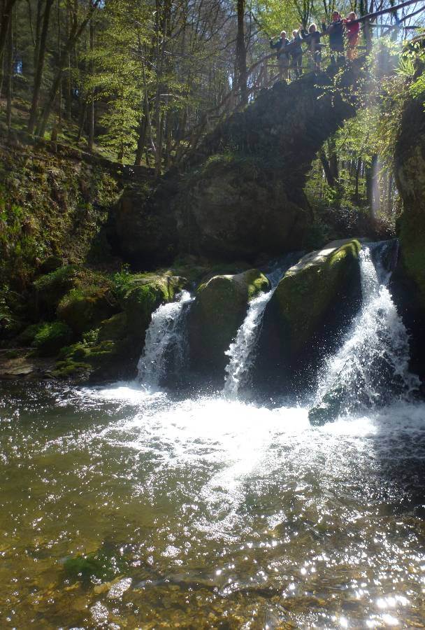 a small waterfall between three rocks and a stone bridge above it