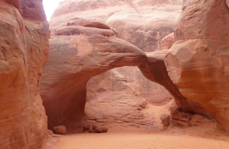 a large red rock formation with an arch through it, the arch is looking worn away and quite thin in one place