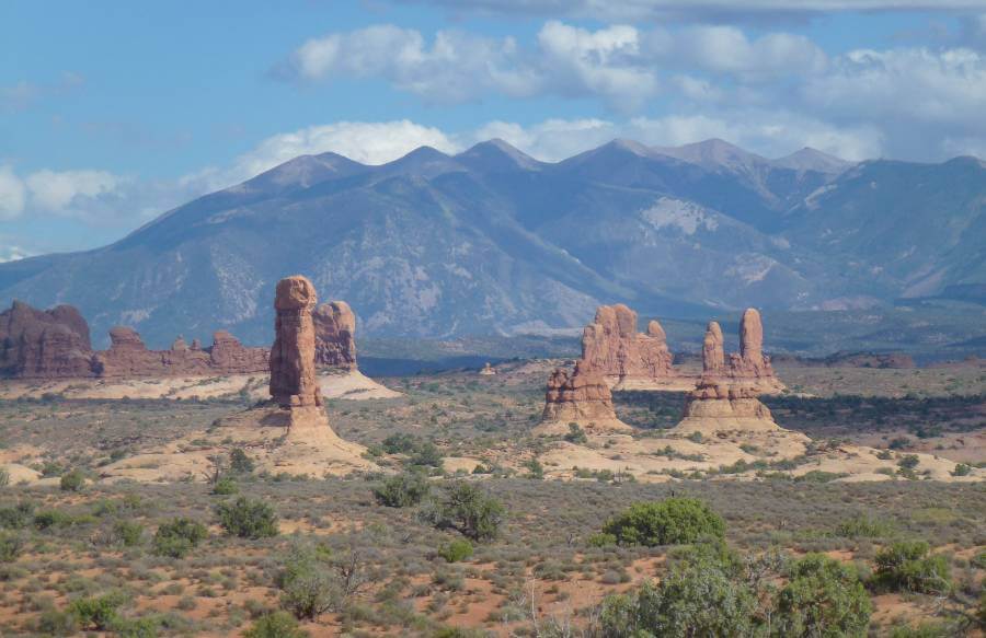 a flat area of orange land with bushes and mountains in the background, with areas of orange rock that have been eroded over millions of years with just parts left