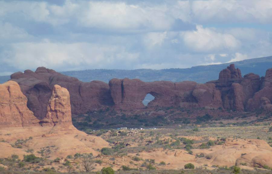 huge large orange rocks sticking up from the ground, that have been worn by the weather over millions of years and in the distance one has a hole through it, with mountains in the background