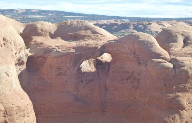 huge large rocks that have been left after millions of years, with holes in them that look like arches, in an orange color with mountains in the background