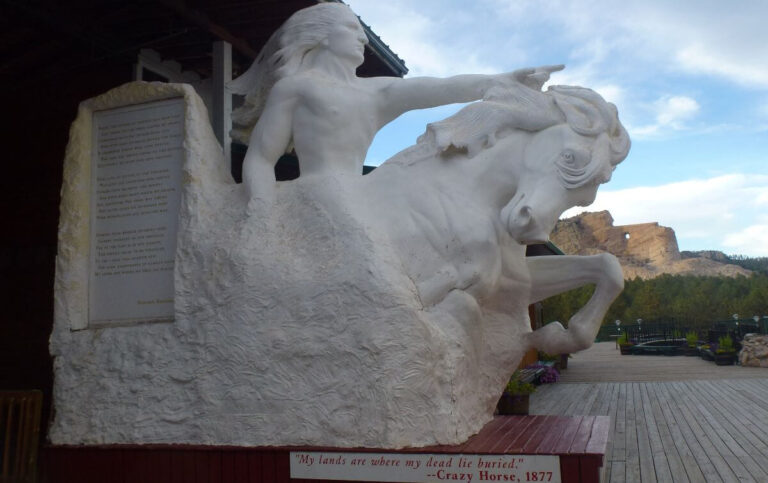 a statue of a man sat on a horse pointing into the distance, with part of the mountain behind it carved to look the same