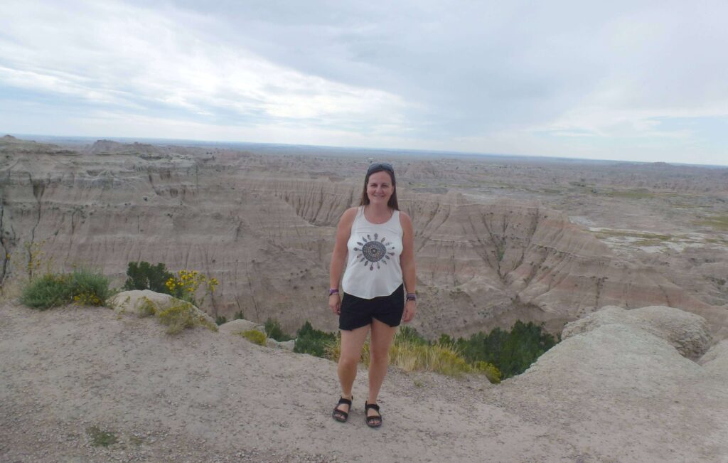 a girl with shorts and tshirt stood in front of a valley of pink and white rock that was been shaped into small valleys over millions of years
