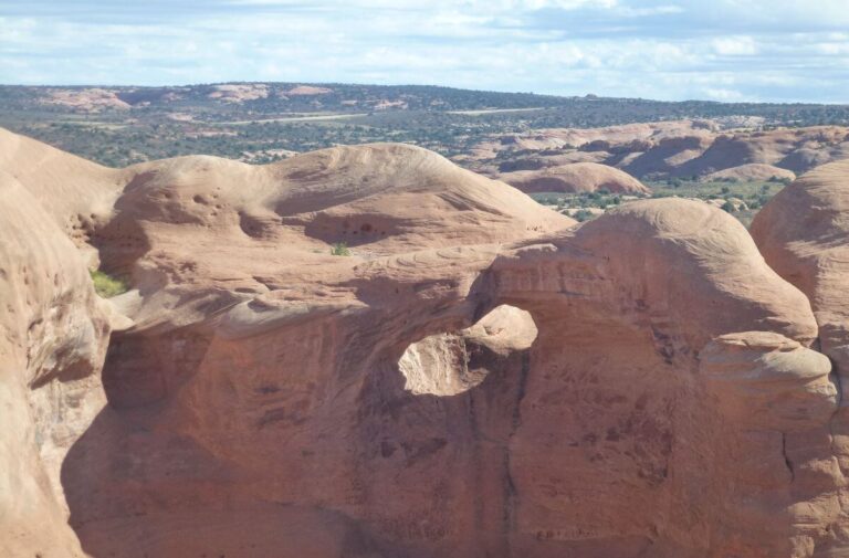 a large area of orange rock that has a hole or an arch through it with mountains in the background