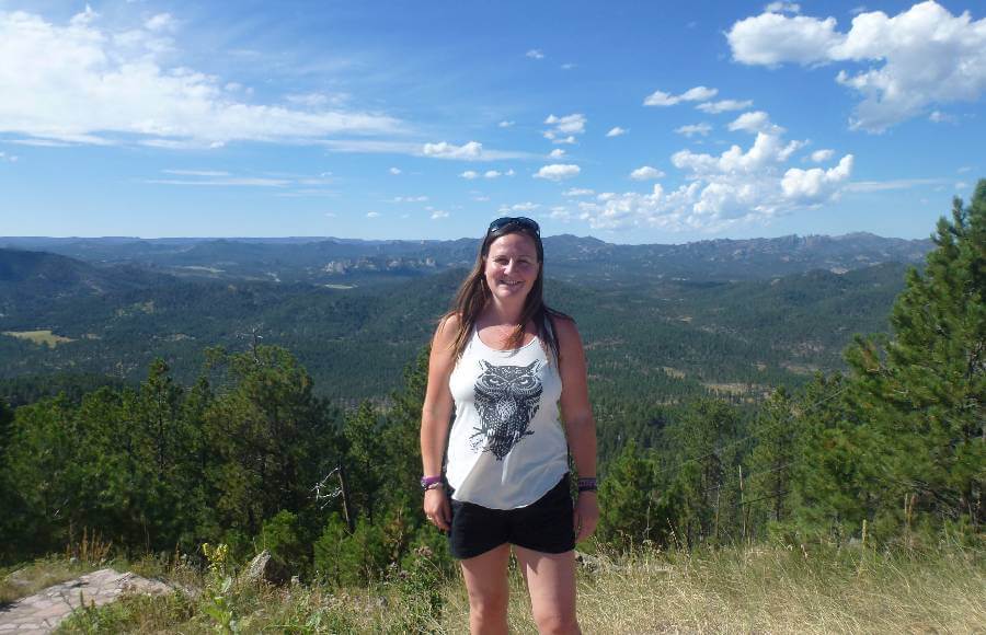 a girl in shorts and tshirt with hills covered in trees behind here and mountains in the background