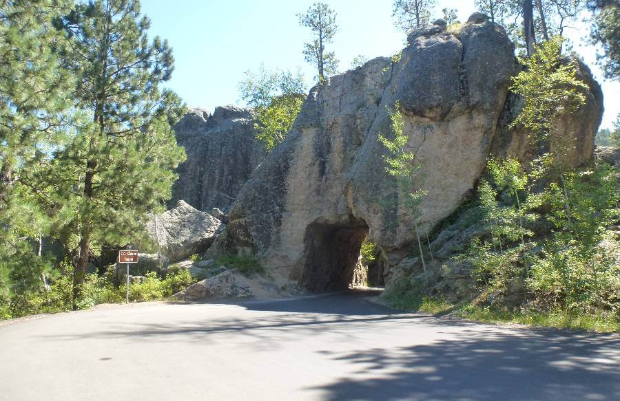 a road going through a hole through a large boulder with trees either side of it