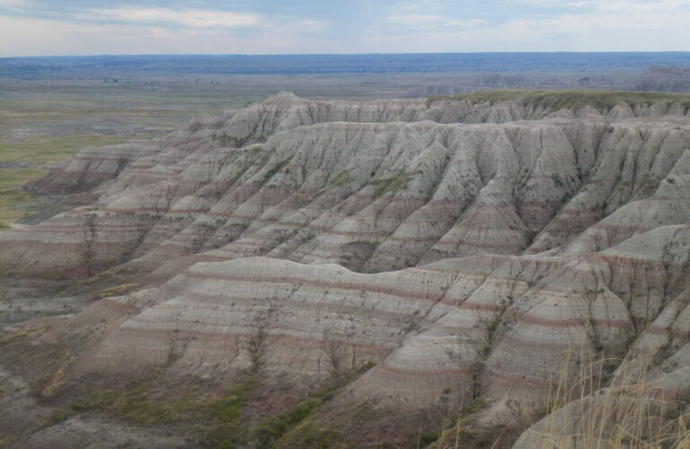 a large area of rock that is pink and white showing the different timeline of thousands of years, there are valleys between the rock down to the floor