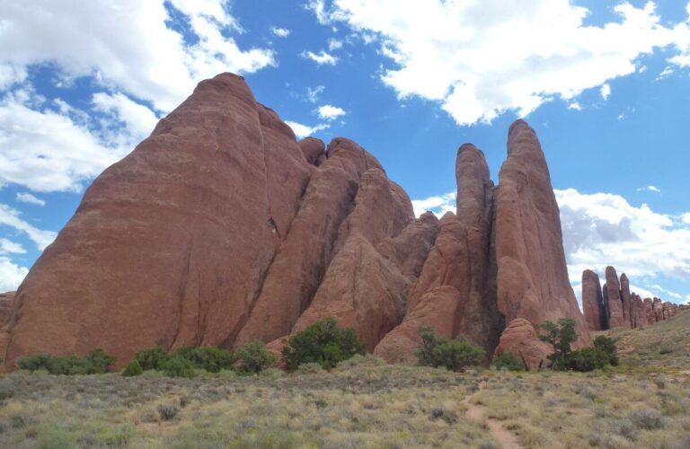 a large rock that has been weathered over the years that is orange with bushes around it