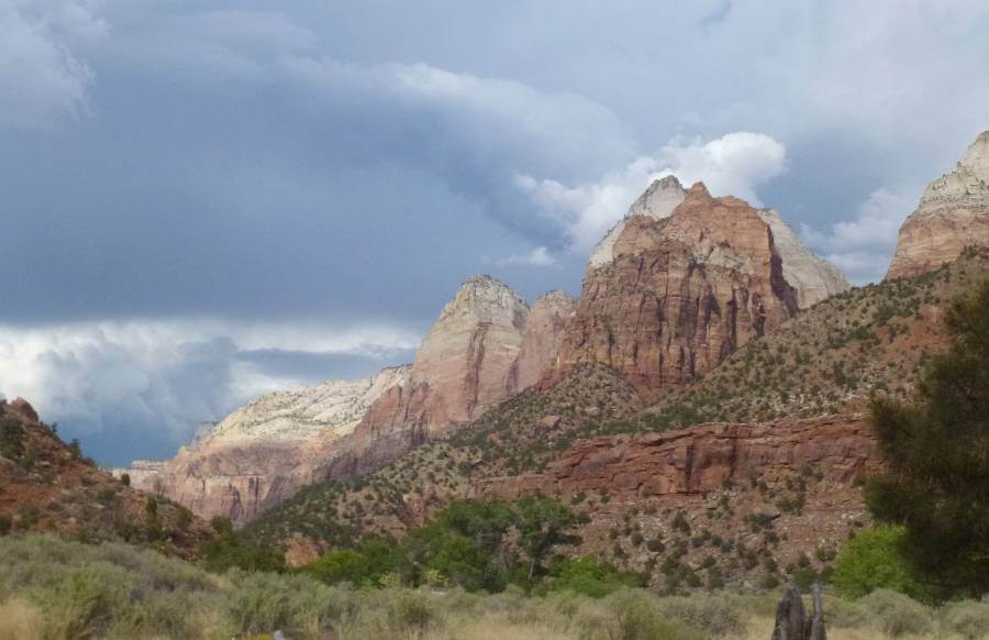 the orange and white canyon walls to the right of the image, with the canyon floor and slopes of the canyon covered in bushes on a cloudy day