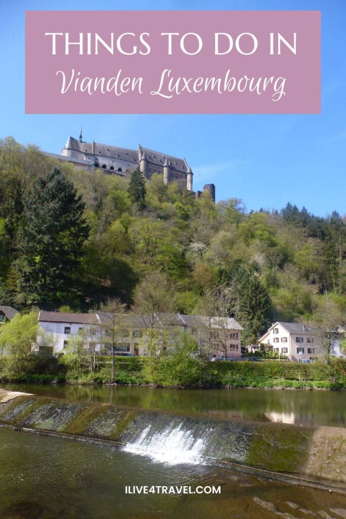 a pinterest pin about things to do in Vianden Luxembourg showing a castle on a hill with trees on the slope down to a river, with houses alongside the river