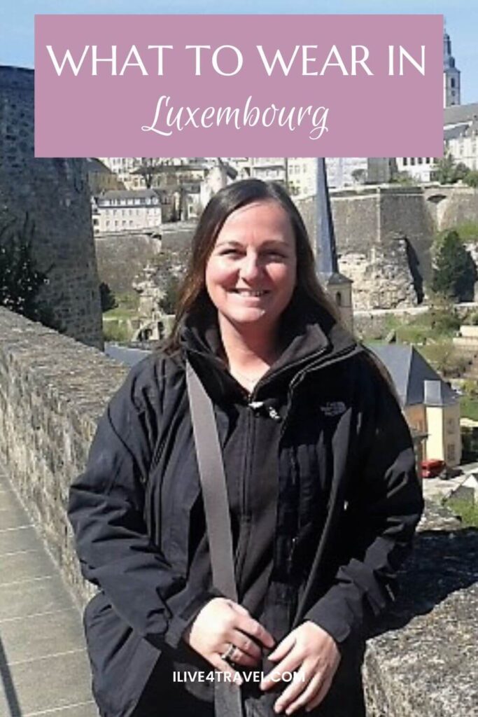 A pinterest pin about what to wear in luxembourg showing a girl dressed in black on an old wall with buildings behind