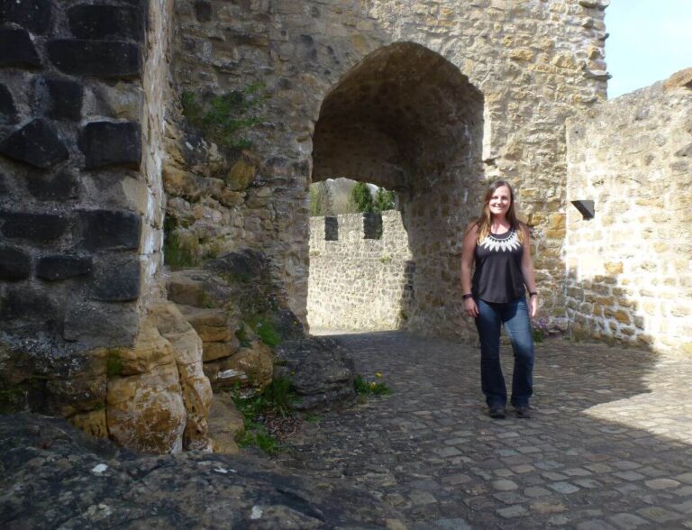 a girl in jeans and a black top with the ruins of a castle gate behind here